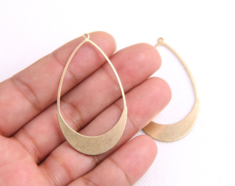 May include: Two gold-toned metal teardrop-shaped earring blanks with a rounded bottom edge. The blanks have a small loop at the top for attaching earring wires.