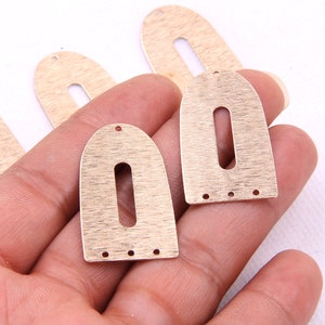 May include: Four gold-colored metal earring blanks with a rounded top and a rectangular opening in the center. Each blank has three small holes along the bottom edge.