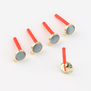 May include: Five gold-toned charms with a gray stone center and a red plastic stick attached. The charms have a loop at the top for attaching to a necklace or bracelet.