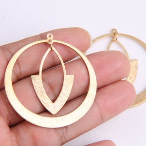 May include: A pair of gold-toned earrings with a geometric design. The earrings are made of metal and have a brushed finish. The earrings are circular in shape and have a smaller, teardrop-shaped cutout in the center.