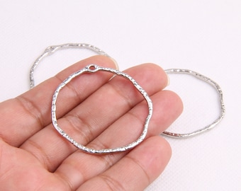 May include: Two silver metal hoops with a textured finish. The hoops are open and have a small hole at the top.