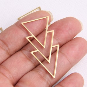 May include: Gold metal triangle shaped pendant with a double layered design. The pendant is held in a hand.