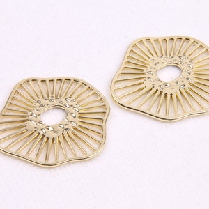May include: Two gold-colored metal earrings with a circular cutout in the center. The earrings are shaped like a flower with a textured surface.