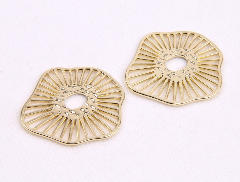 May include: Two gold-colored metal earrings with a circular cutout in the center. The earrings are shaped like a flower with a textured surface.
