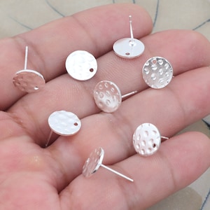 May include: Silver earring blanks with a textured, circular design. The blanks have a small hole in the center and a post on the back.