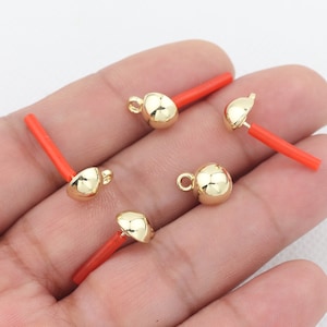 May include: Five gold-colored metal bead caps with a loop on top and a red plastic stick attached to the bottom.