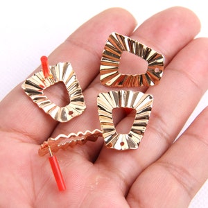Peut inclure: Quatre breloques d'oreille en métal de couleur dorée avec un design festonné et un trou pour fixer un crochet ou une tige.