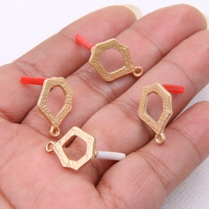 Puede incluir: Cuatro colgantes de metal de color dorado con forma hexagonal y superficie texturizada. Cada colgante tiene un pequeño bucle en la parte superior para sujetarlo a una cadena o cordón.