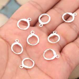 May include: Ten silver jump rings, each with a small loop on one side. The rings are arranged on a hand, with some overlapping.