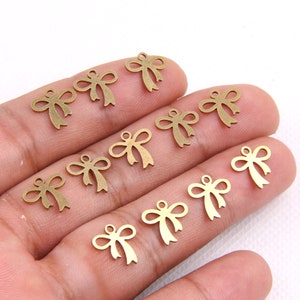 May include: A collection of 10 gold-toned metal bow charms. The charms are in the shape of a bow with a loop at the top for attaching to jewelry or other crafts.