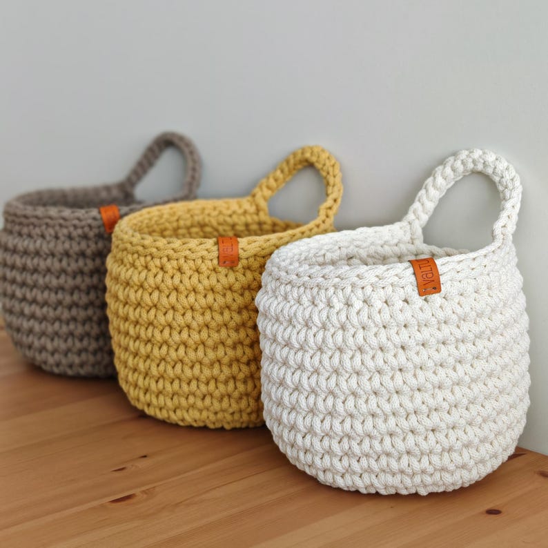 Pu&ograve; includere: Tre cesti appesi in crochet di colore beige, giallo e bianco. Ogni cesto ha un'etichetta in pelle con la parola "Little" su di essa.