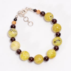 Peut inclure: Un bracelet composé de perles rondes vertes, jaunes et brunes. Le bracelet a un fermoir argenté.