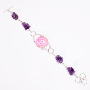 Pode incluir: Pulseira de prata com uma pedra de ágata rosa e detalhes em ametista. A pulseira tem um fecho de correr.