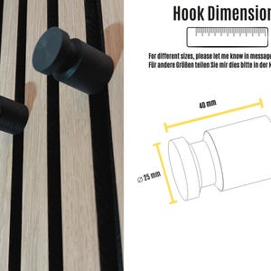Black matte 3D-printed hook mounted on a wooden acoustic panel, supporting up to 4 kg for coats and backpacks