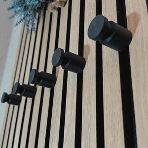 Minimalist knob hook for slatted acoustic panels, easy to install without screws or drilling, ideal for modern interiors.