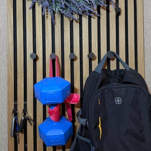 Black matte 3D-printed hook mounted on a wooden acoustic panel, supporting up to 4 kg for coats and backpacks