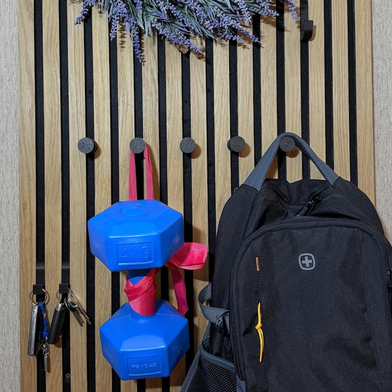 Black matte 3D-printed hook mounted on a wooden acoustic panel, supporting up to 4 kg for coats and backpacks