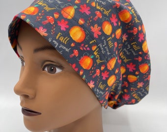 May include: A dark gray scrub cap with a repeating pattern of orange pumpkins, red and orange leaves, and mushrooms. The words "Fall is my second favorite word" are printed on the cap. The cap is designed for medical professionals.