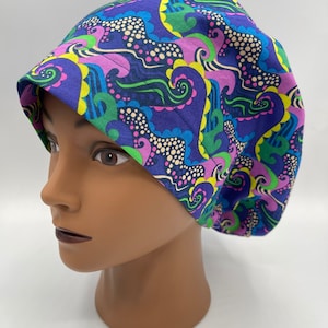 May include: A purple, green, yellow and pink patterned scrub hat with a swirl design.