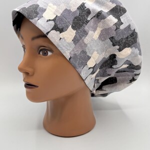 May include: A gray and white camouflage patterned scrub hat. The hat is made of a soft, comfortable fabric and has a tie at the back.