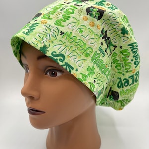 May include: Green and gold patterned scrub hat with a variety of St. Patrick's Day themed text and images, including shamrocks, leprechauns, and pots of gold.