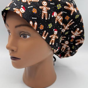 Puede incluir: Un gorro de quirófano negro con un patrón de esqueleto de jengibre. El gorro tiene una cuerda blanca para atar.
