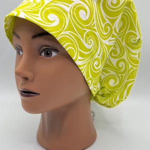 Puede incluir: Un gorro de quirófano amarillo y blanco con estampado de espirales. El gorro está hecho de una tela suave y cómoda y está diseñado para ser usado por profesionales médicos.
