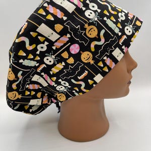 May include: Black scrub hat with a Halloween themed print featuring candy corn, pumpkins, bats, and ghosts.
