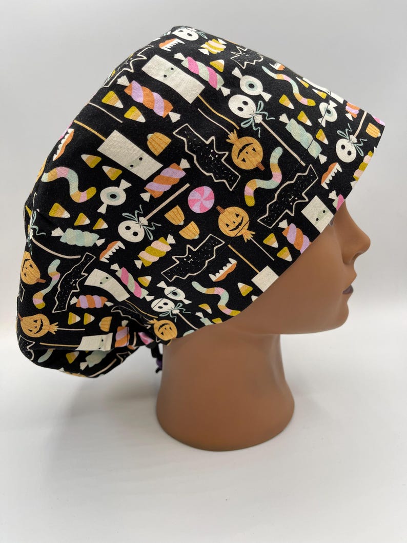May include: Black scrub hat with a Halloween themed print featuring candy corn, pumpkins, bats, and ghosts.