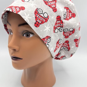 May include: A gray and red patterned scrub hat with the text "Oh, Fudge!" repeated throughout. The hat has a white snowflake pattern and a red and black plaid design.