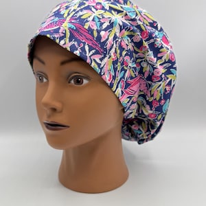 May include: A navy blue scrub cap with a floral pattern featuring pink, green, and yellow accents. The cap is displayed on a mannequin head.