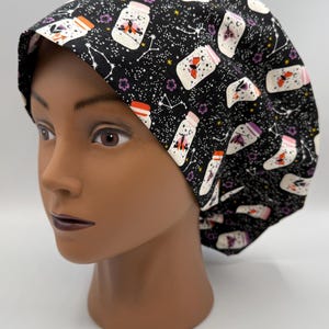 May include: Black surgical scrub cap with a whimsical pattern of jars, butterflies, constellations, and flowers. The jars have red, pink, and white accents. The cap is on a mannequin head.
