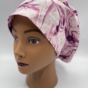May include: A white and purple swirl patterned scrub hat. The hat is made of a soft, comfortable fabric and is designed to be worn by medical professionals.