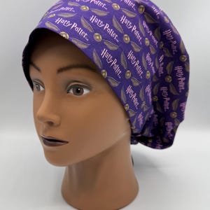 May include: A purple scrub cap featuring a repeating pattern of the words "Harry Potter" and golden snitch illustrations. The cap is designed to fit snugly and is made of a soft, flexible material.