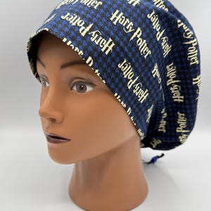 Op de afbeelding: Een blauw en zwart patroon operatiemuts met de woorden "Harry Potter" in een herhalend patroon. De muts staat op een mannequinhoofd. De muts heeft een trekkoord en een witte voering.