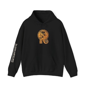 May include: A black hooded sweatshirt featuring a gold-colored graphic of an Egyptian-style profile on the chest. The right sleeve displays the white text: The ancient world isn't dead. You've just not been properly introduced.