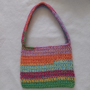 Op de afbeelding: Een veelkleurige gehaakte tote bag met een lange band. De tas is gemaakt van verschillende kleuren, waaronder groen, blauw, oranje, geel en roze.