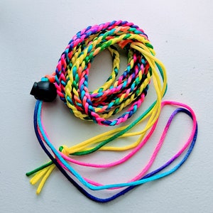 May include: A coiled, multi-colored braided cord with a black plastic clasp. The cord features a vibrant array of colors, including pink, yellow, blue, and green. Several loose strands of the same colors extend from the clasp, creating a playful and eye-catching design.