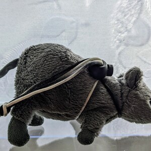 May include: A plush gray mouse toy with a long tail and black whiskers. The toy has a harness made of black, white, and gray cords. The mouse is approximately 6 inches long.