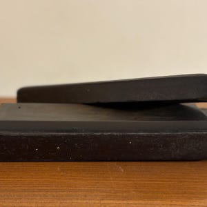 May include: A dark grey ink stone with a rectangular base and a matching lid. The lid is slightly angled, resting on the base. The ink stone is likely used for calligraphy or traditional East Asian art.