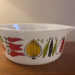 May include: A white glass mixing bowl with a pouring spout and a repeating graphic pattern of colourful vegetables including red peppers, a yellow onion, green pea pods, and red apple halves outlined in black lines around the exterior surface.