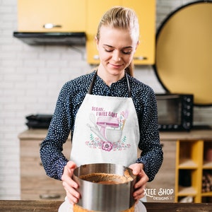 May include: A white apron with the text "Today I will bake" and a pink mixer design. The apron is worn by a person in a kitchen, holding a cake with a metal ring. The kitchen has yellow cabinets and a black oven.