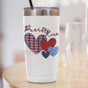 May include: White insulated travel mug with a black straw and a silver lid. The mug features the words "Puerto Rico" in red script above four heart designs. The hearts are red, blue, and white with patriotic patterns.