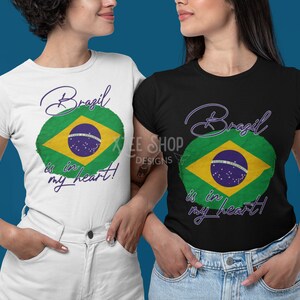 以下が含まれることがあります： ブラジル国旗のデザインのTシャツを着た2人の女性。シャツは白と黒で、「Brazil is in my heart!」というテキストが筆記体で書かれています。ブラジルの国旗は緑、黄、青、白です。