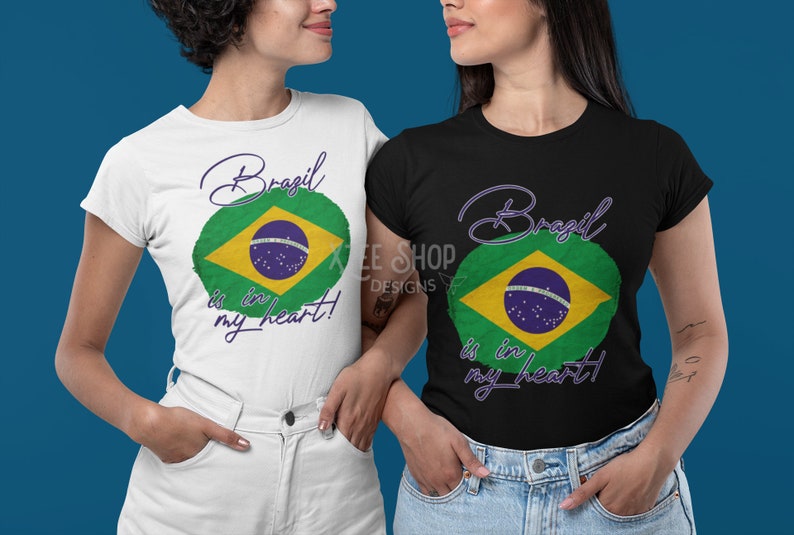 以下が含まれることがあります： ブラジル国旗のデザインのTシャツを着た2人の女性。シャツは白と黒で、「Brazil is in my heart!」というテキストが筆記体で書かれています。ブラジルの国旗は緑、黄、青、白です。