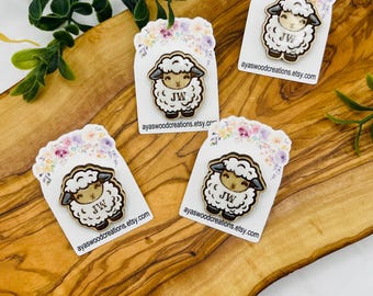 May include: Four wooden sheep pins with white wool, brown accents, and the initials "JW" are displayed on white cards with floral designs. The cards are arranged on a wooden surface, with the website address ayaswoodcreations.etsy.com printed on each card.