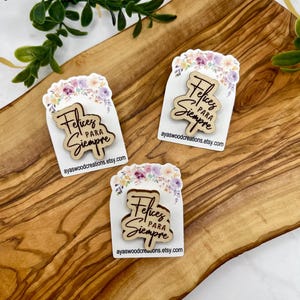 Könnte beinhalten: Drei Holzpins mit dem Schriftzug "Felices Para Siempre" in Schreibschrift. Jeder Pin befindet sich auf einer weißen Karte mit einem floralen Design oben. Die Website-Adresse ayaswoodcreations.etsy.com ist unten auf jeder Karte aufgedruckt.