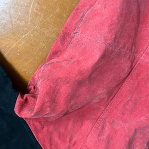 Puede incluir: Primer plano de una prenda roja y negra. La secci&oacute;n roja tiene un aspecto texturizado y descolorido con costuras visibles. La secci&oacute;n negra es lisa y contrasta con el rojo. La prenda parece estar hecha de un material suave.