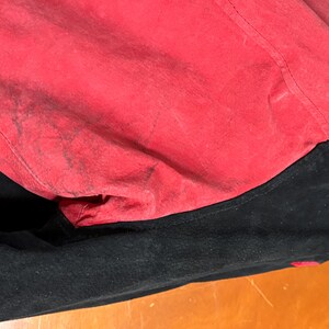 Puede incluir: Primer plano de una chaqueta negra con forro rojo. El forro rojo es visible, mostrando una superficie texturizada con manchas m&aacute;s oscuras. La chaqueta parece ser de ante o un material similar.