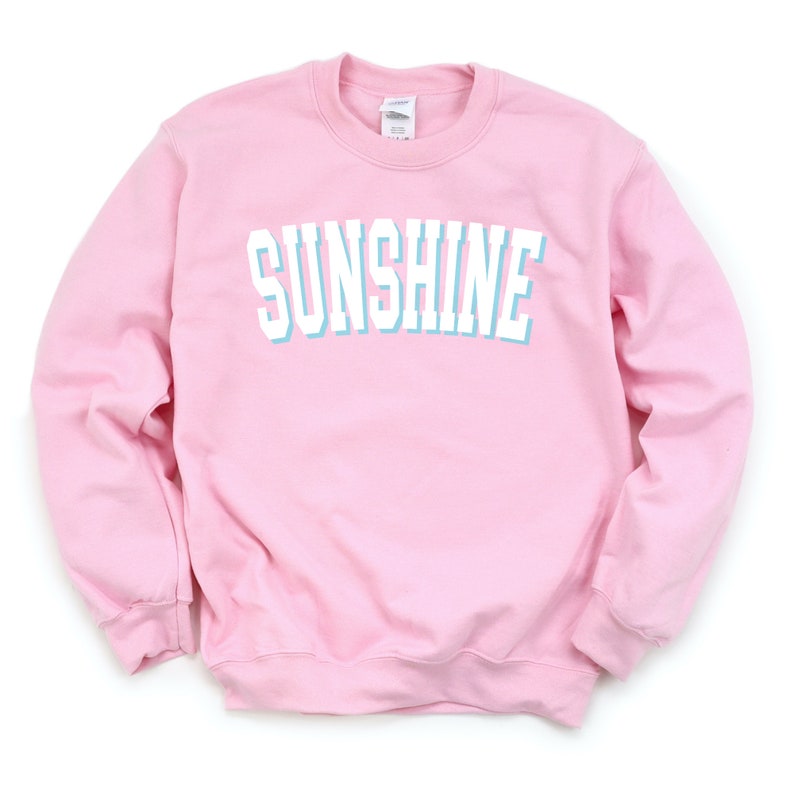 Peut inclure: Un sweat-shirt rose avec le mot "SUNSHINE" imprim&eacute; en blanc avec un contour bleu clair.